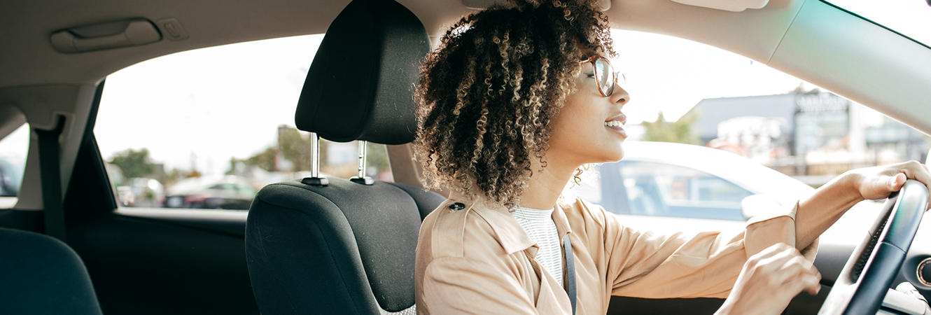 Woman smiling while driving her car through traffic.