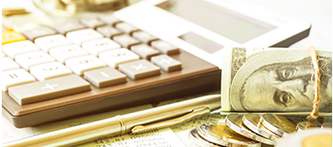 A calculator, pen, gold coins, and roll of money laying on a table. 