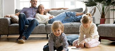 Mom and dad lounging on a couch as their son and daughter play on the floor.